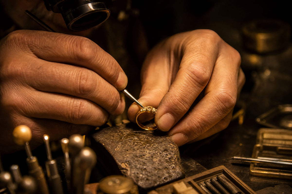Jeweler working on a gold ring at a workbench surrounded by hand tools